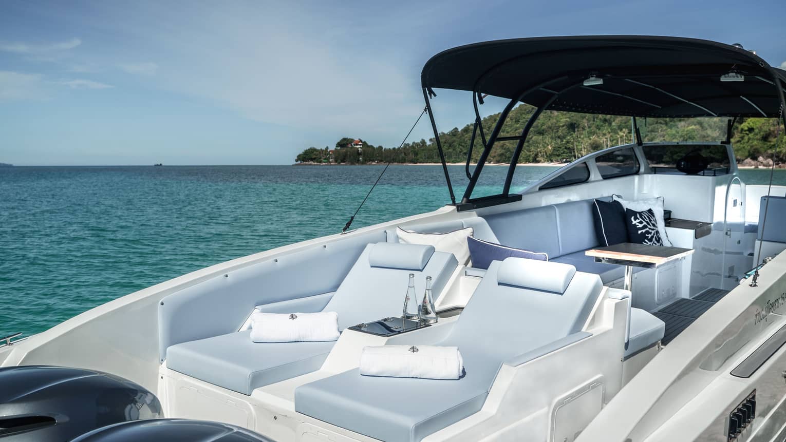 Interior view of a luxurious speedboat furnished with lounge chairs; the ocean, beaches and jungle stretch into the distance.