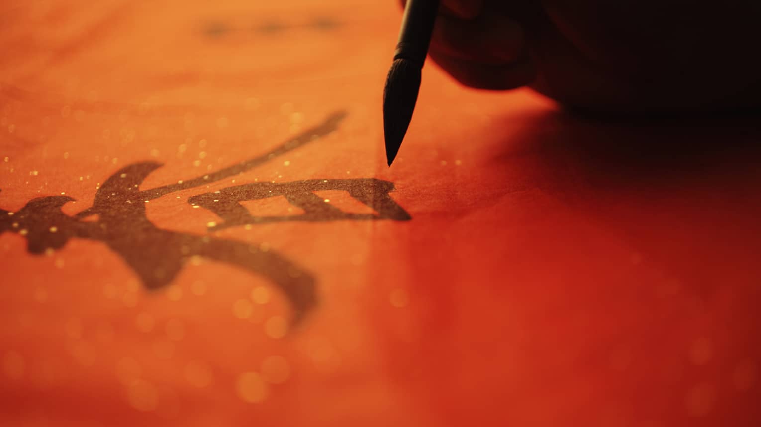 Close up of a hand painting a Chinese graphic on a red background 