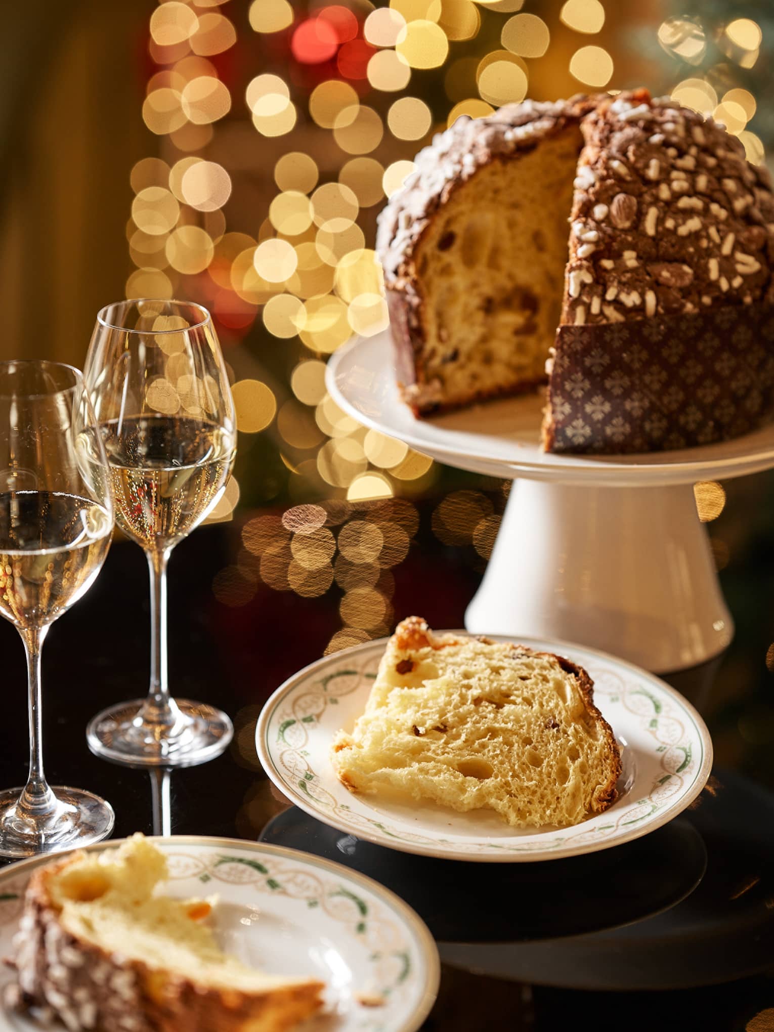 Panettone on stand with slices on plates and two glasses of champagne