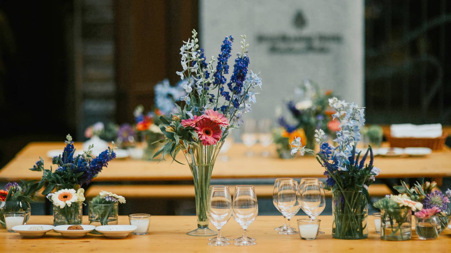 Row of small vases of flowers on table with small wine glasses
