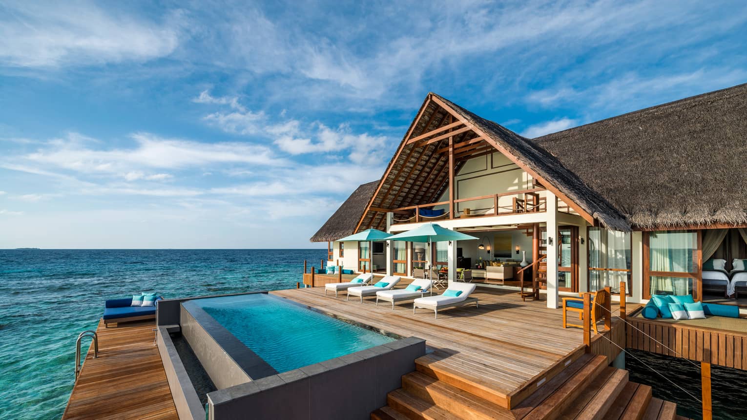 Sunset Two-Bedroom Water Suite with thatched roof, lounge chairs on large patio by pool