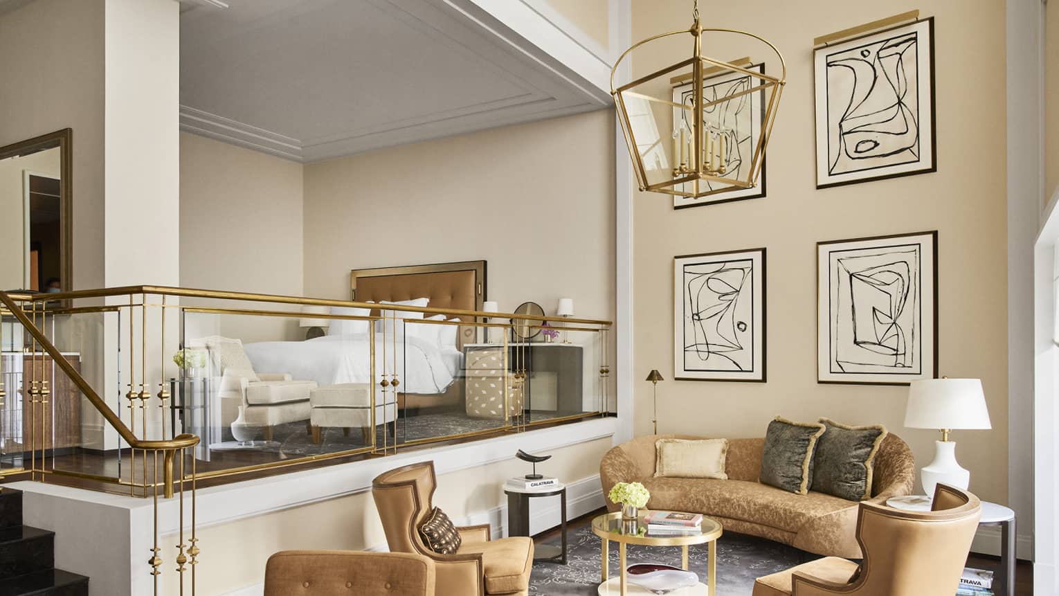Luxury hotel loft suite with a raised king bed, armchair with ottoman, gold railing, sitting area with plush sofa, armchairs, coffee table and abstract wall art