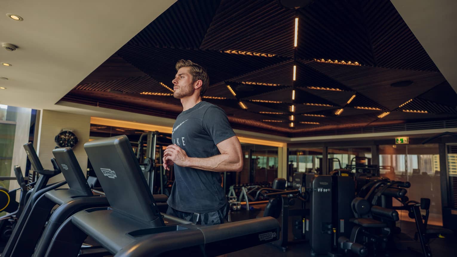 Man wearing dark grey t-shirt and shorts runs on a treadmill in a hotel gym
