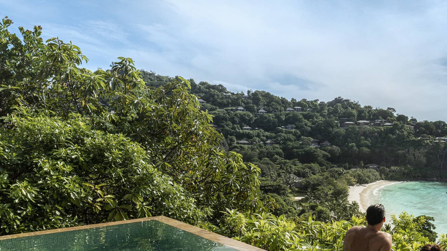 A couple looks out at a view of crystal blue waters and cliffs from an infinity pool