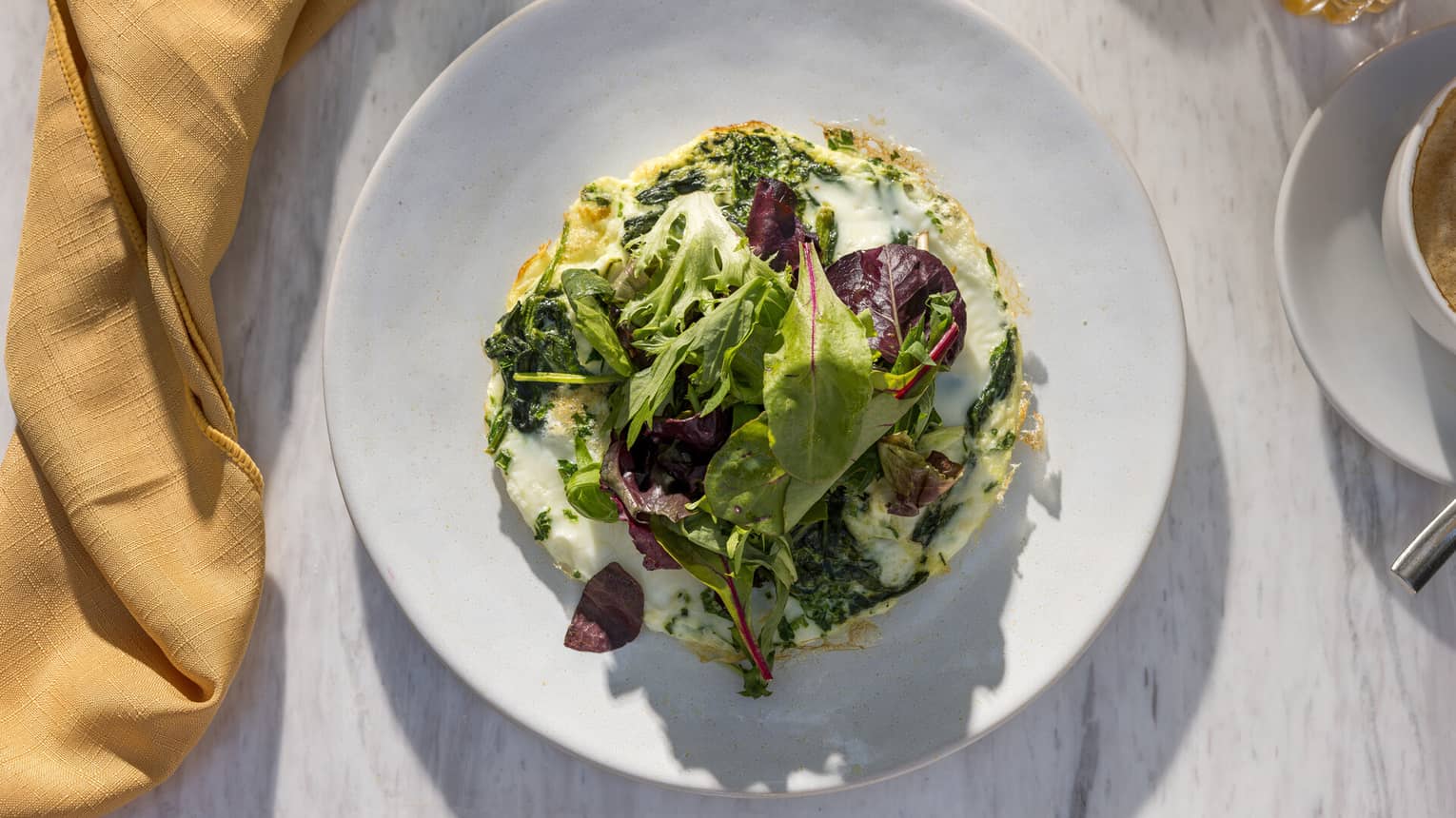 A colourful egg dish topped with greens, served on a white dish