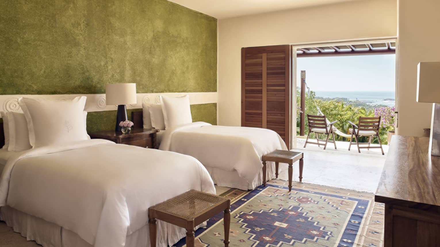 Bedroom with two twin beds, green accent wall, small benches, walk-out terrace