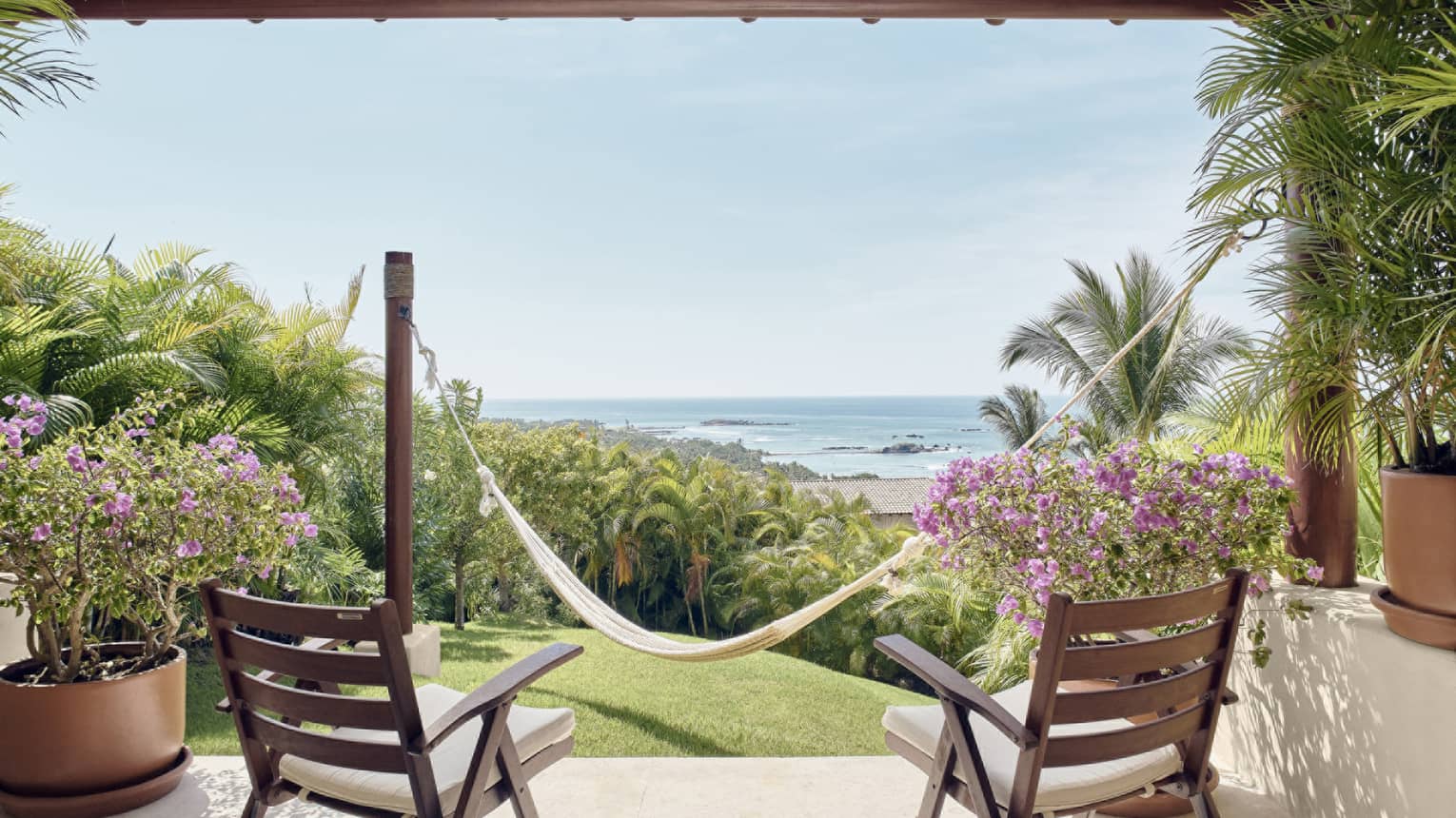 Private terrace with two wooden chairs, hammock on small grass yard, ocean view