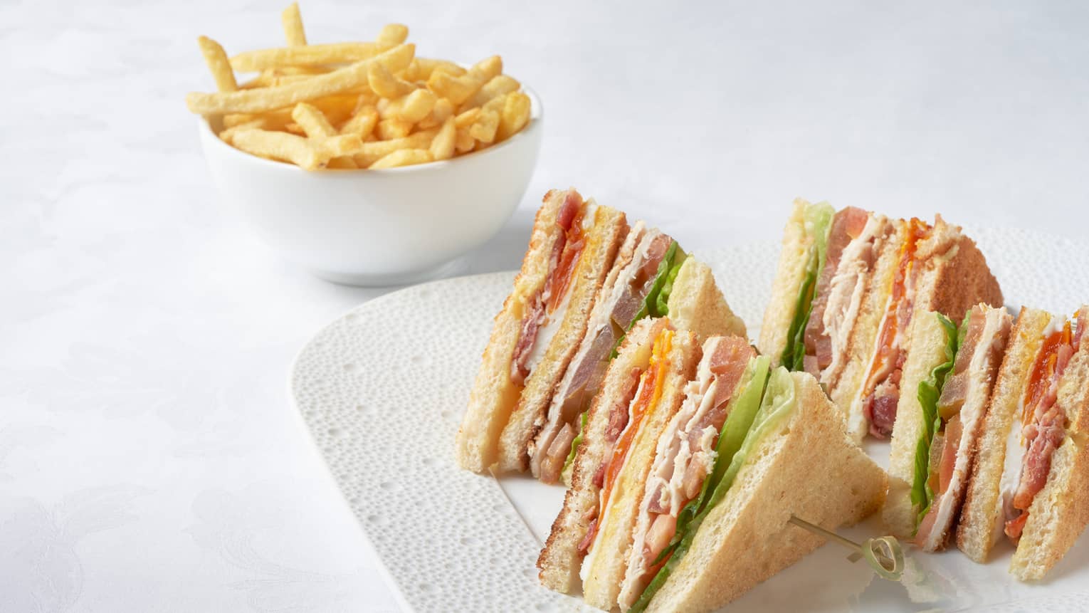 Club sandwich on white plate and fries in white bowl