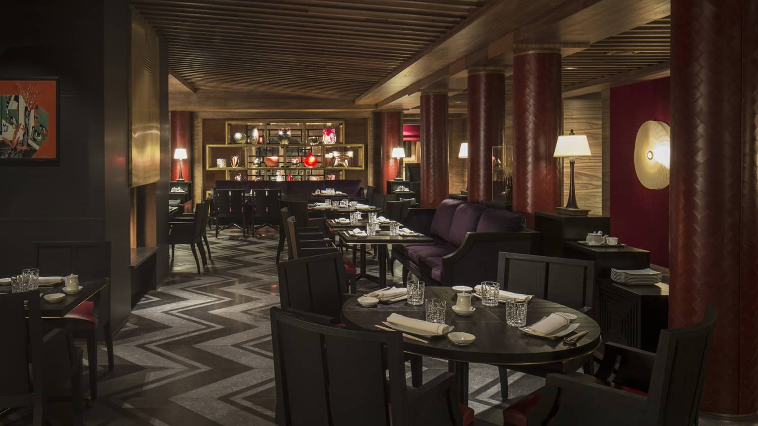 Kaito dimly-lit dining room with round tables, chairs, purple banquettes, red pillars