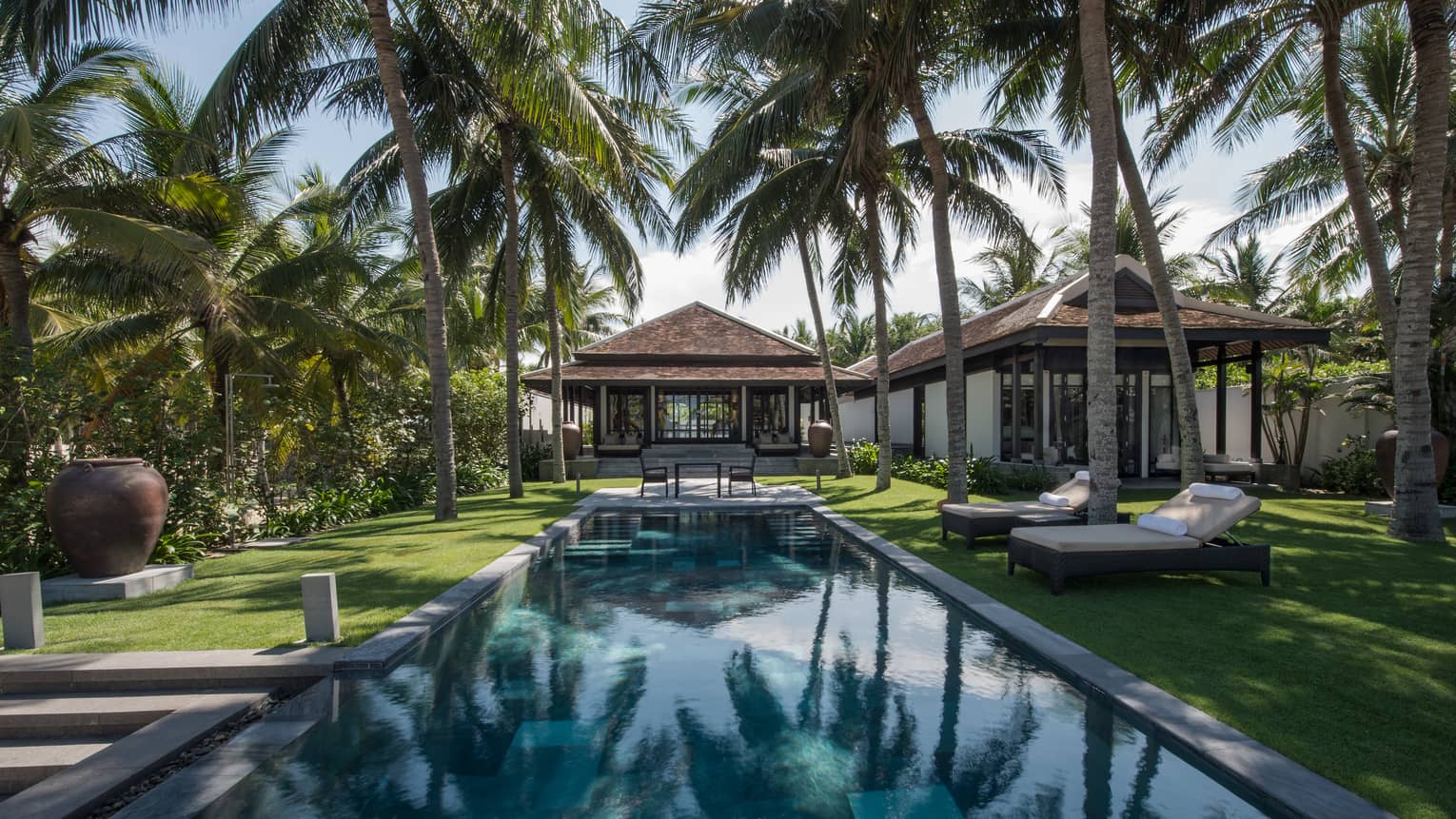 Pool villa, small patio table at end of outdoor swimming pool under palms