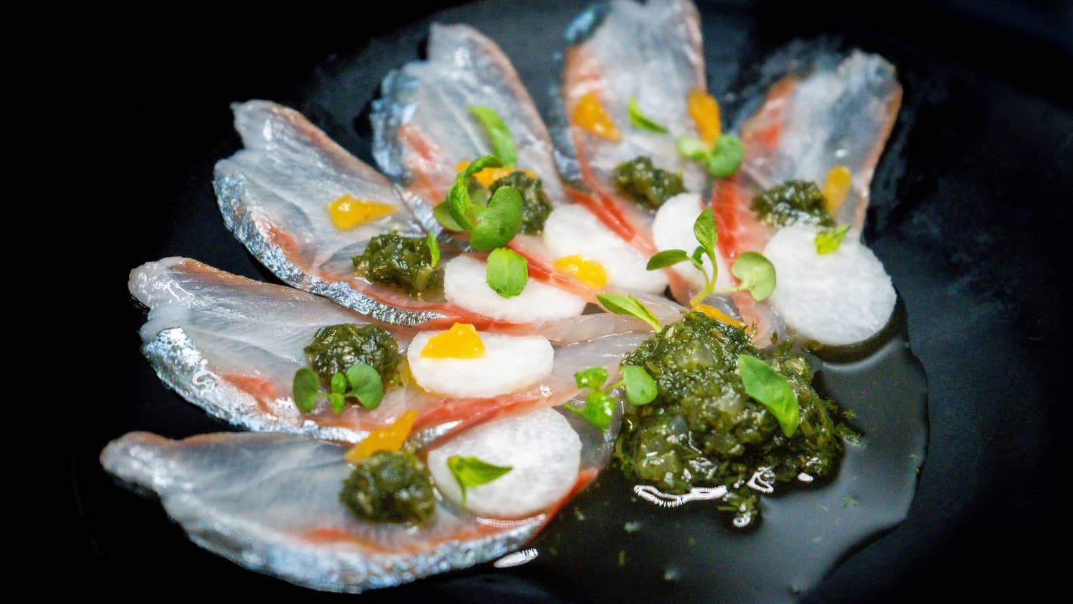 Colourful food items and green garnishes on a black plate