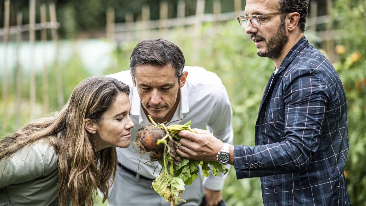 A man and woman lean in to smell a root vegetable in the garden