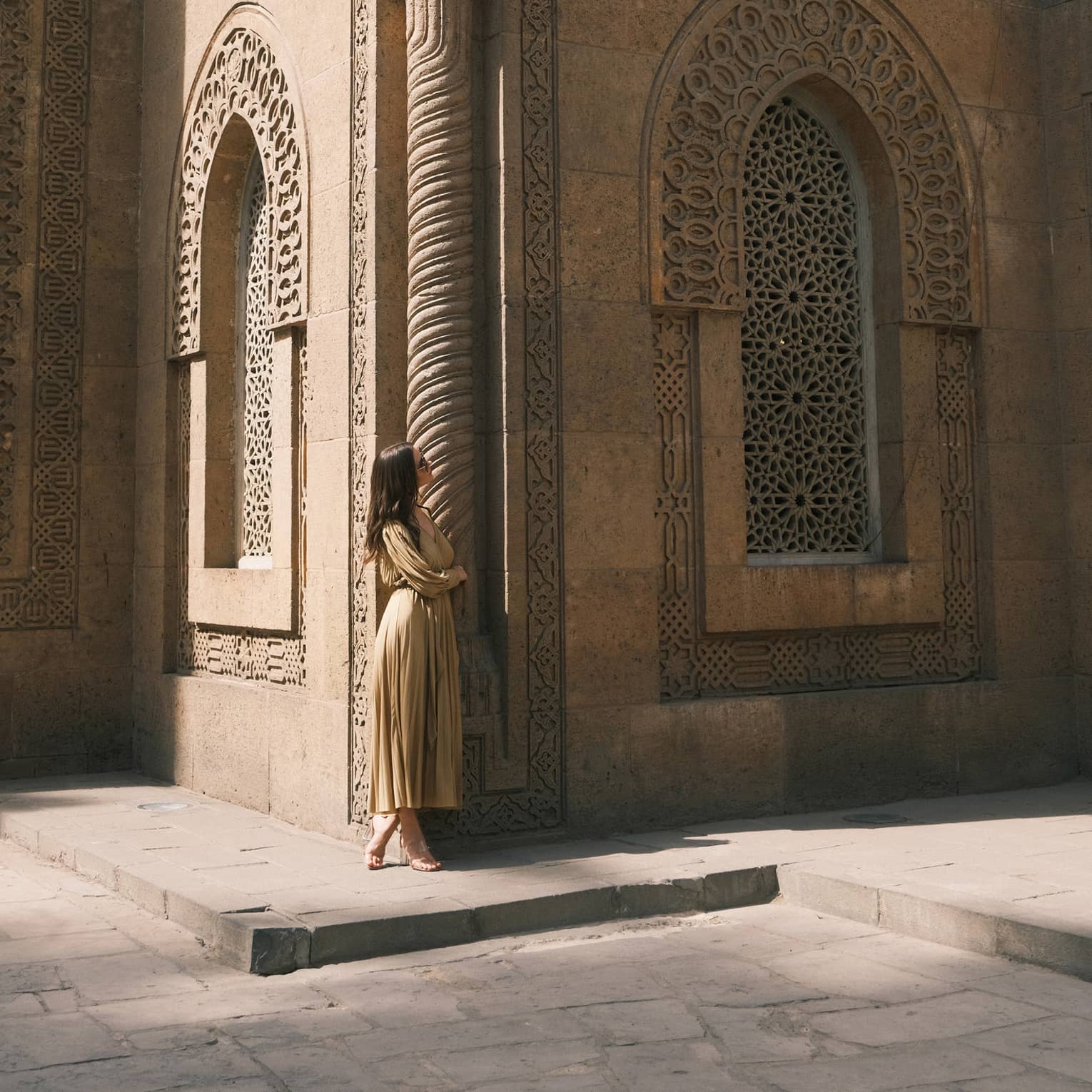 A guest looks up at an ornately carved building featuring a spiral column and arched windows with honeycomb latticework.