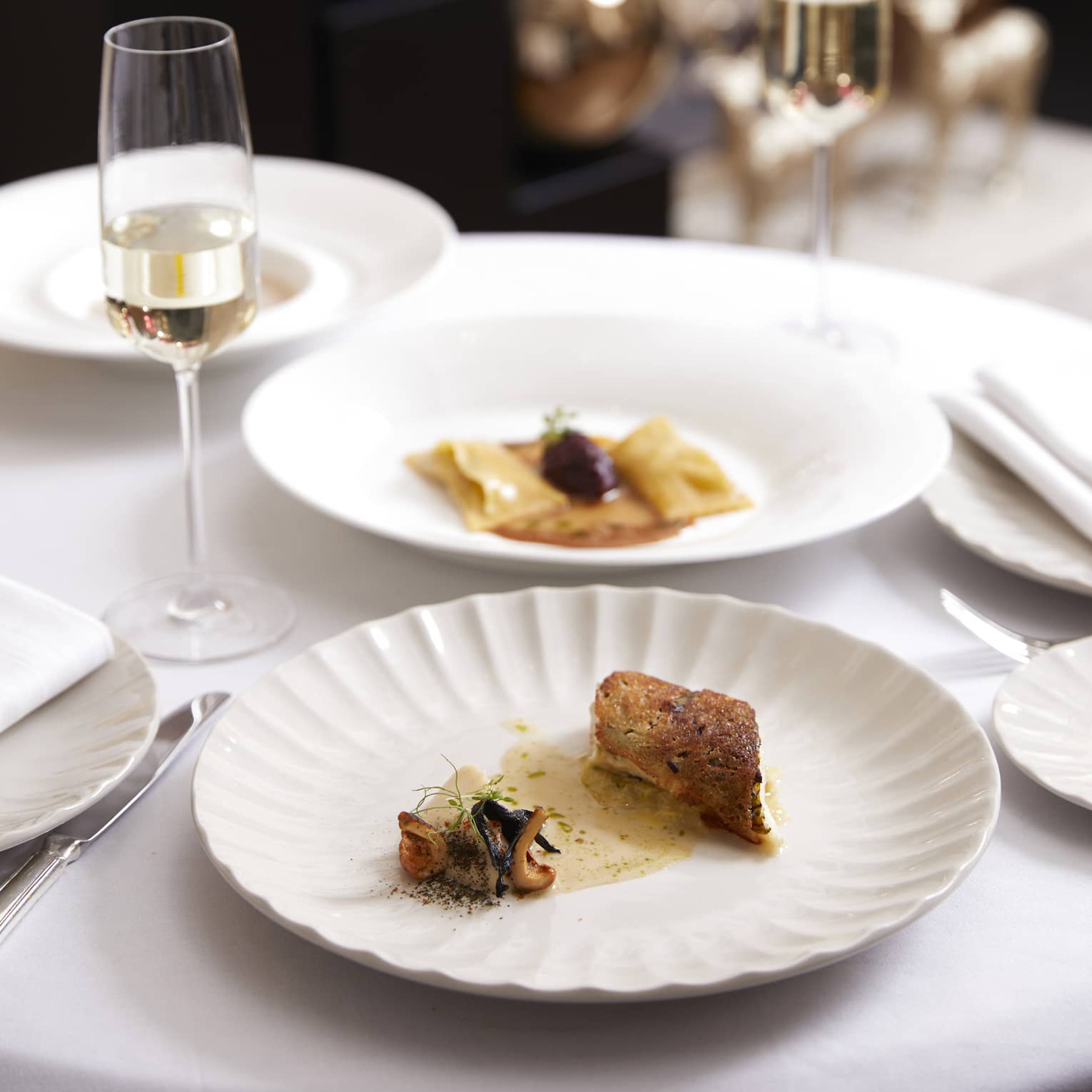 Two white plates with small sauced dishes and two champagne flutes with holiday decor in backdrop