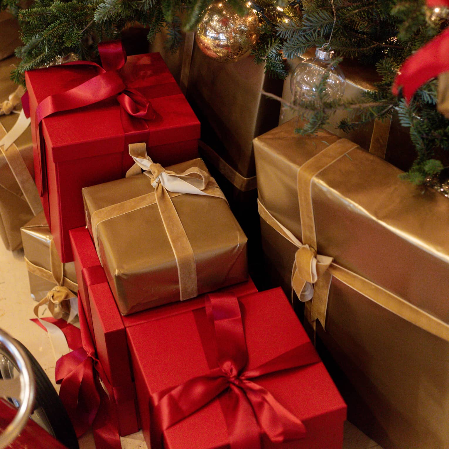 Close-up of red and gold gift boxes with bows under a Christmas tree decorated with red and gold ornaments.