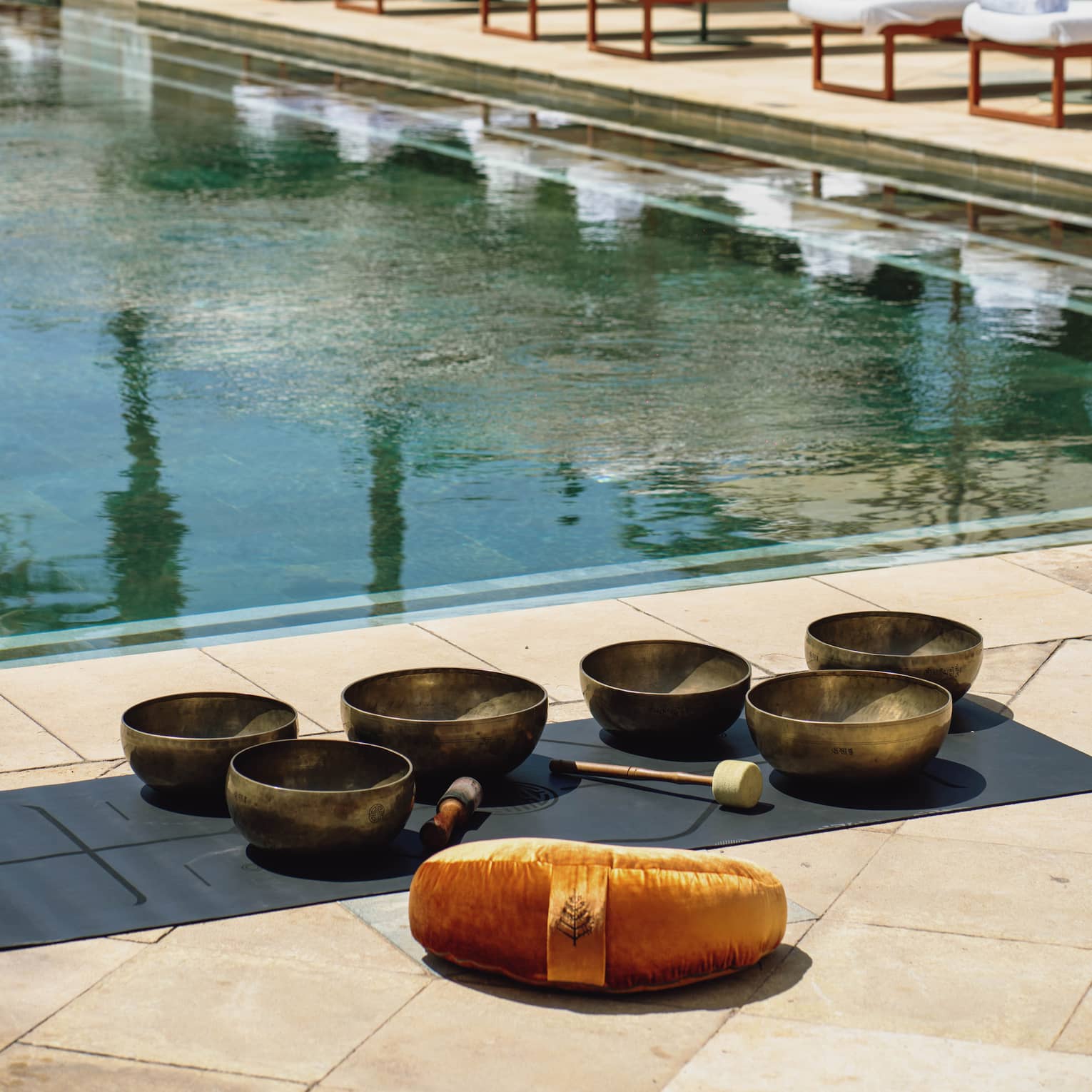 Sound healing bowls in front of a pool and white lounge chairs with umbrellas