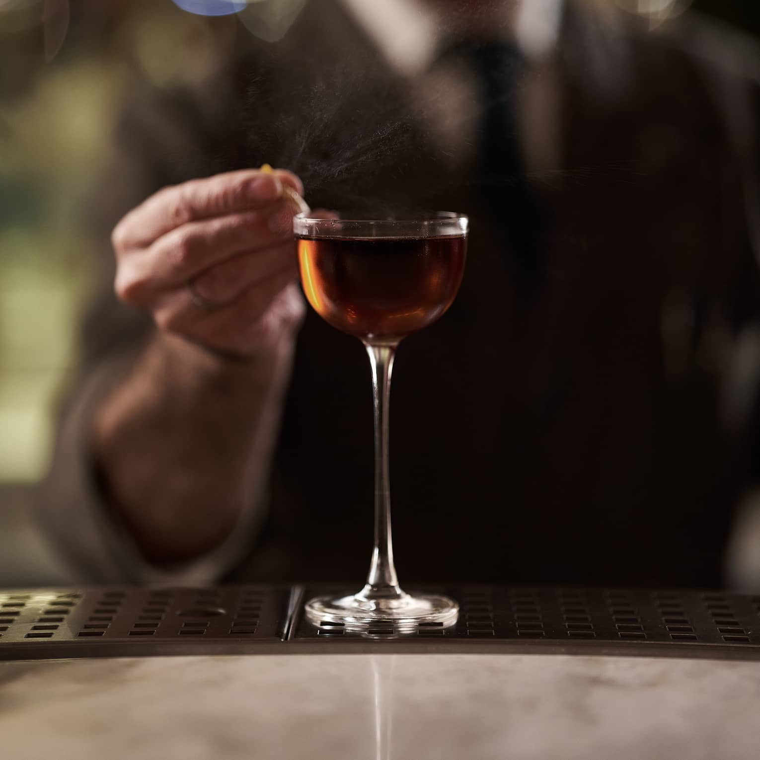 Bartender in suit garnishing a tall amber-coloured cocktail