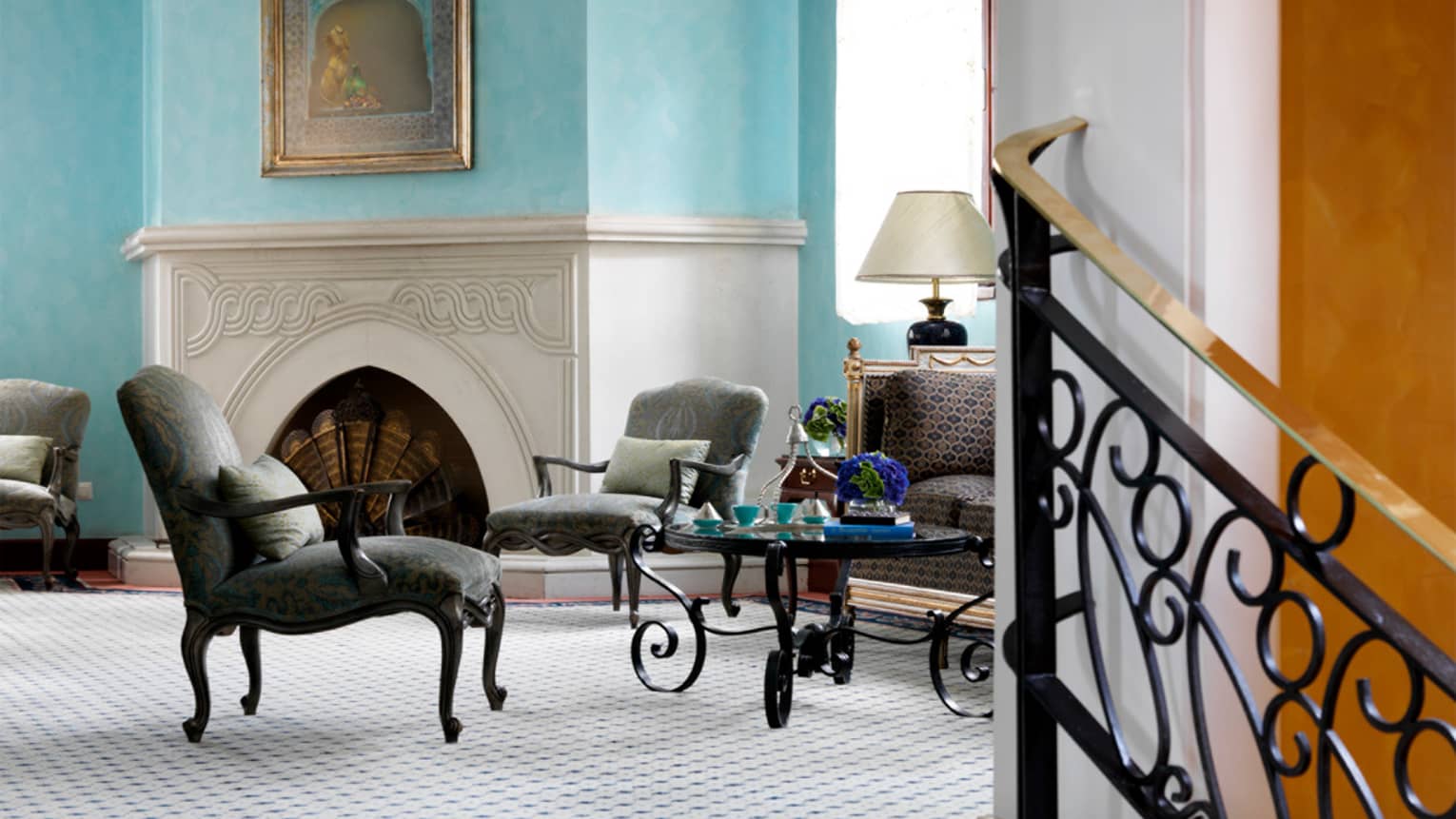 Dark dining chairs around small glass table in Lounge, near white fireplace mantle