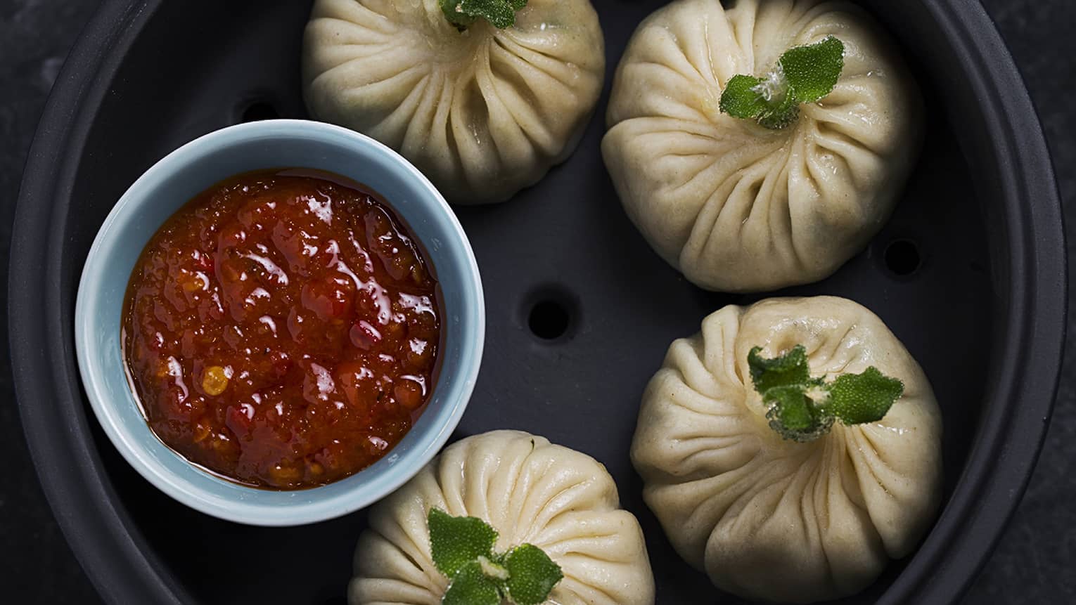 Four Chicken Dimsum and a bowl of red sauce in a black stone bowl