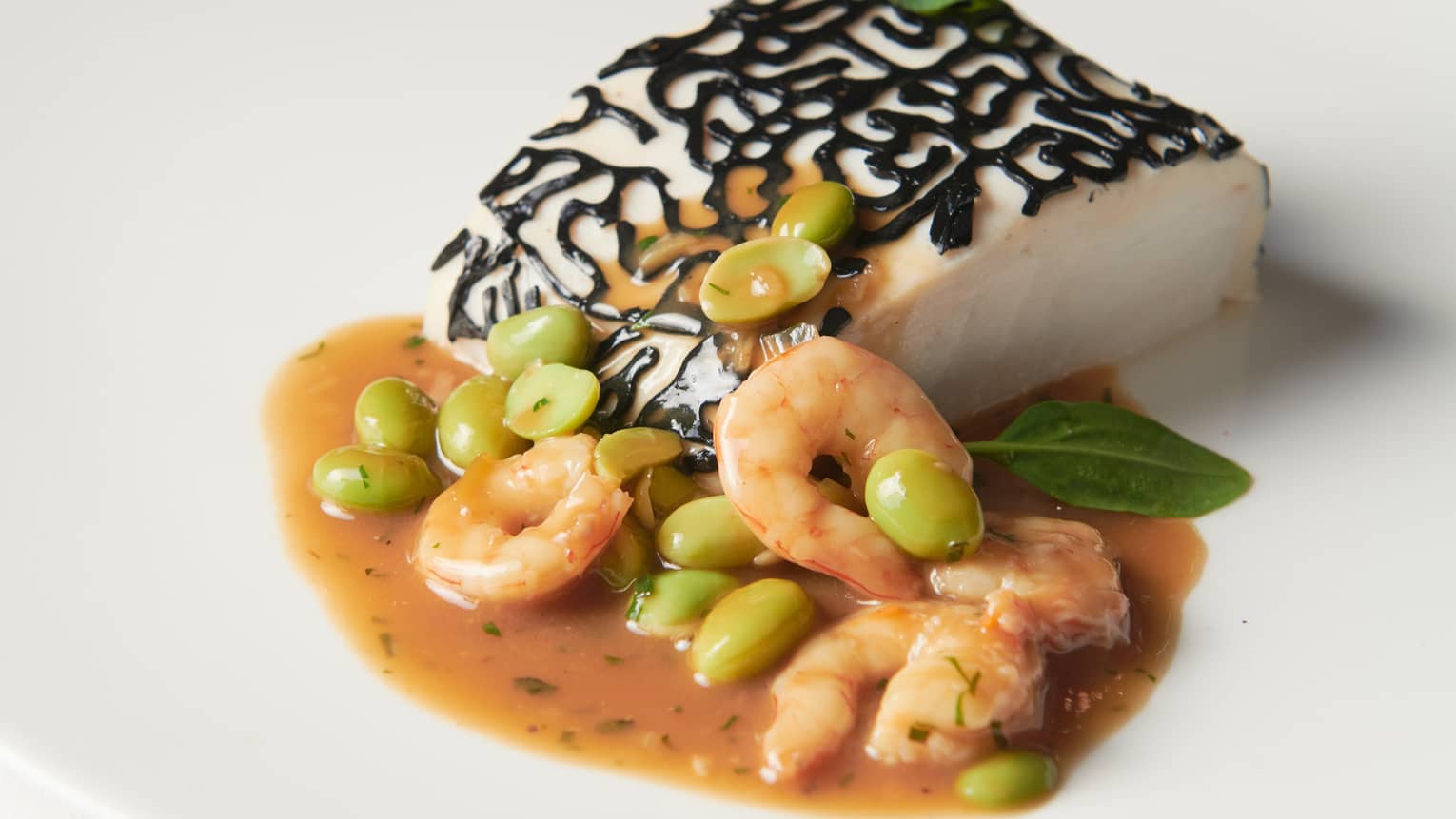Hake with Shrimp, Reduced Poultry Jus and Edamame on round white plate
