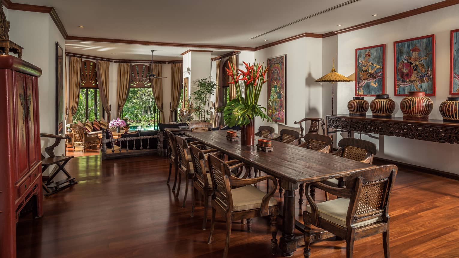 Long wood dining table with vase with tall tropical flowers in bright room