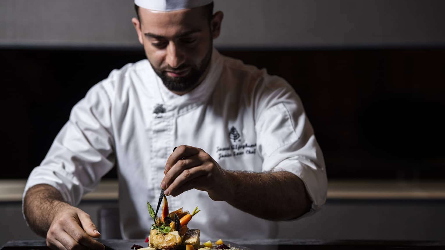 A chef places a garnish on a dish