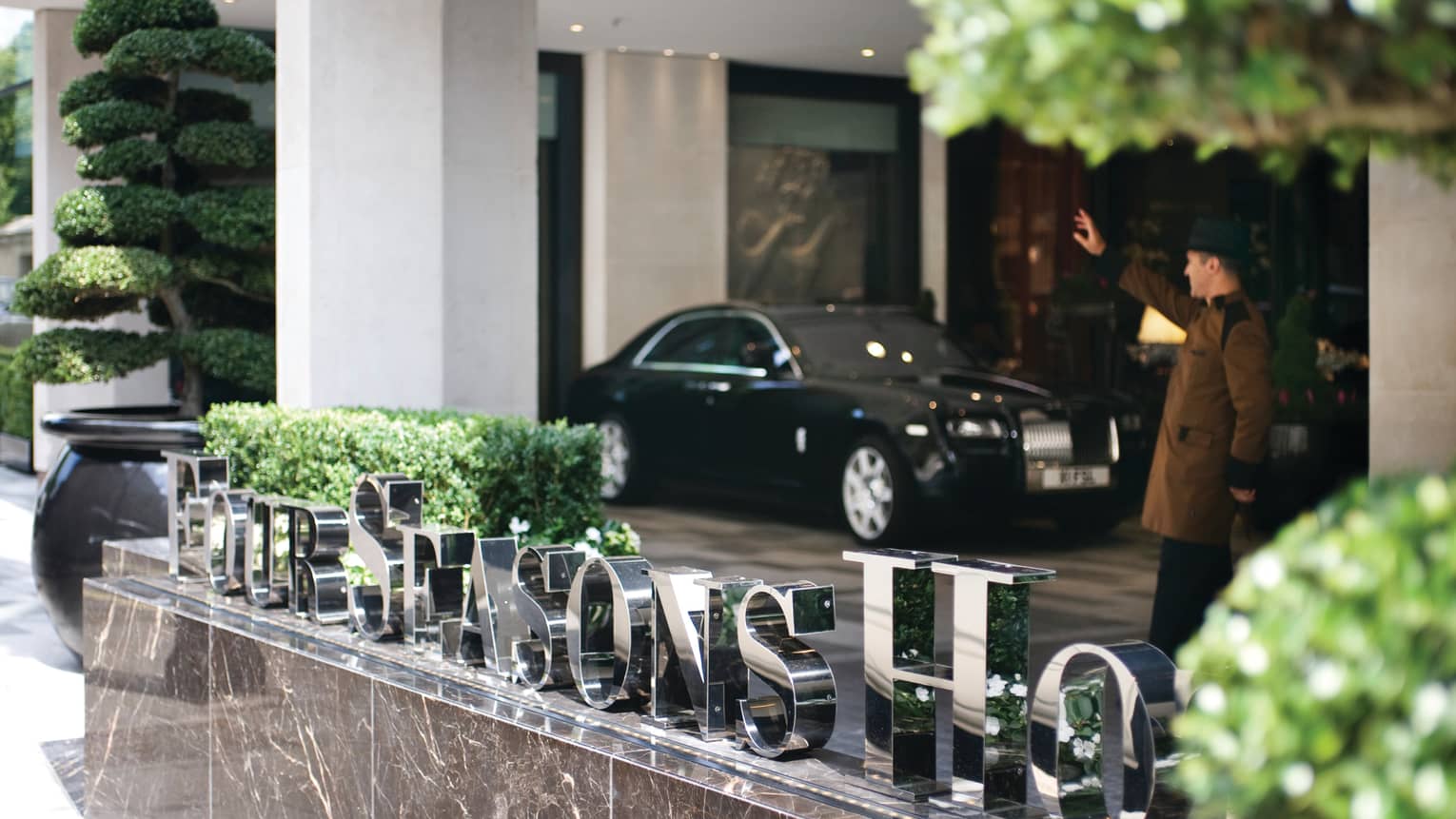 Steel Four Seasons Hotel sign on marble by doorman in uniform, black luxury car