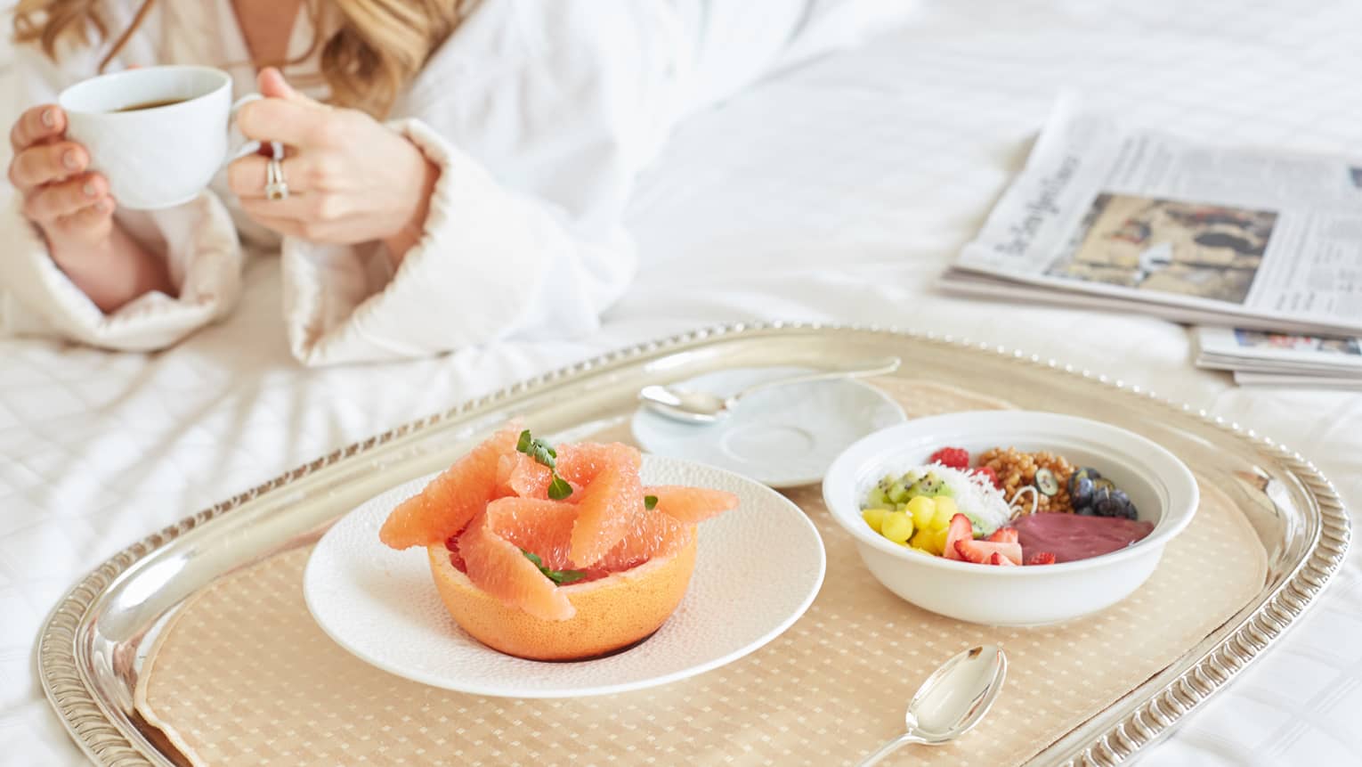 In-room dining tray with grapefruit, granola bowl, woman in bathrobe with coffee