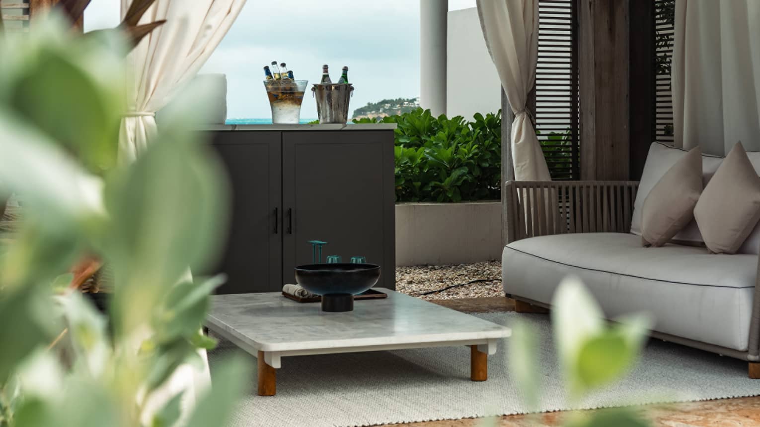 A cabana with a marble table and couch surrounded by palm trees