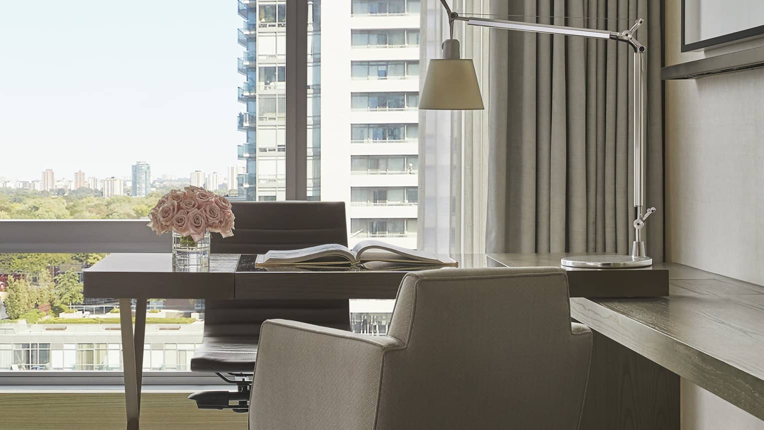 Guest room office area with desk, swivel chair, arm chair and reading lamp, floor-to-ceiling window, views of downtown Toronto