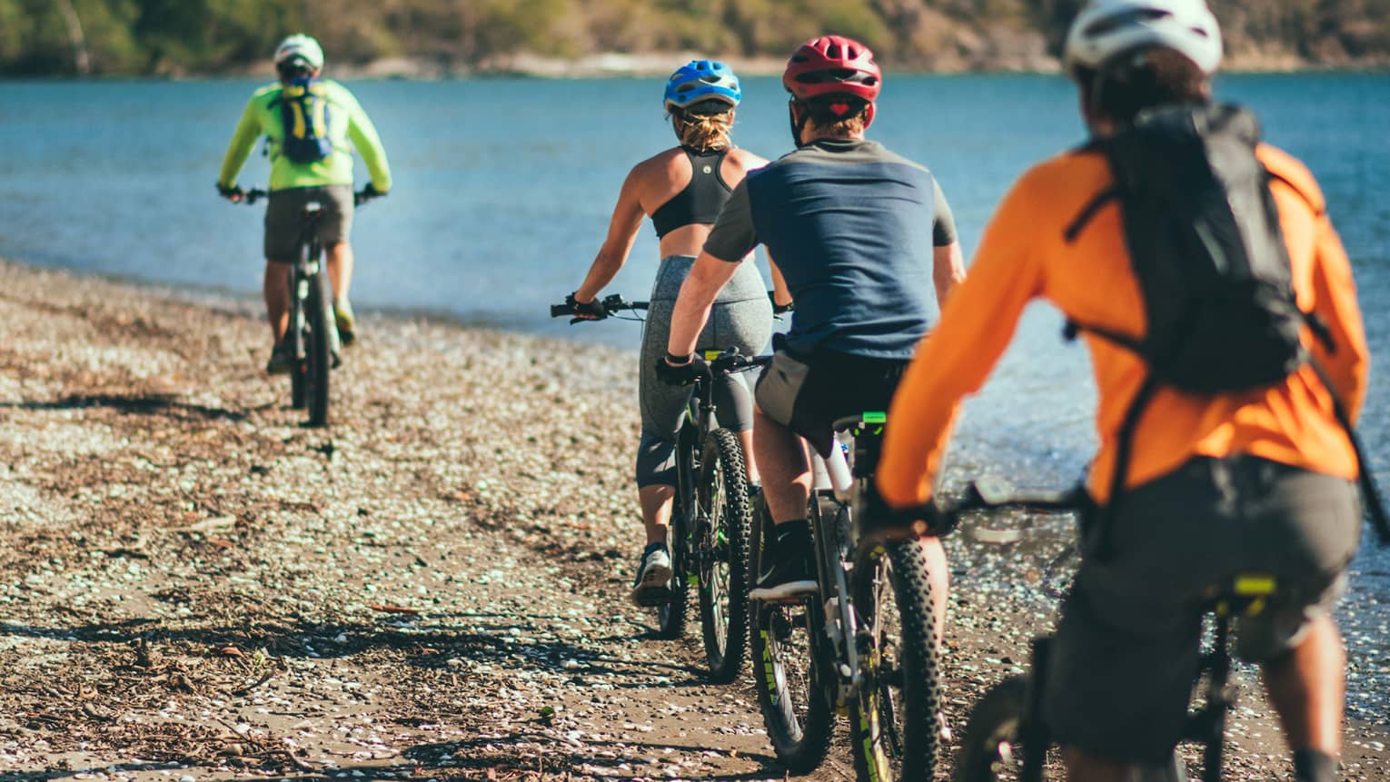 Four people riding bicycles through a rocky terrain next to the ocean