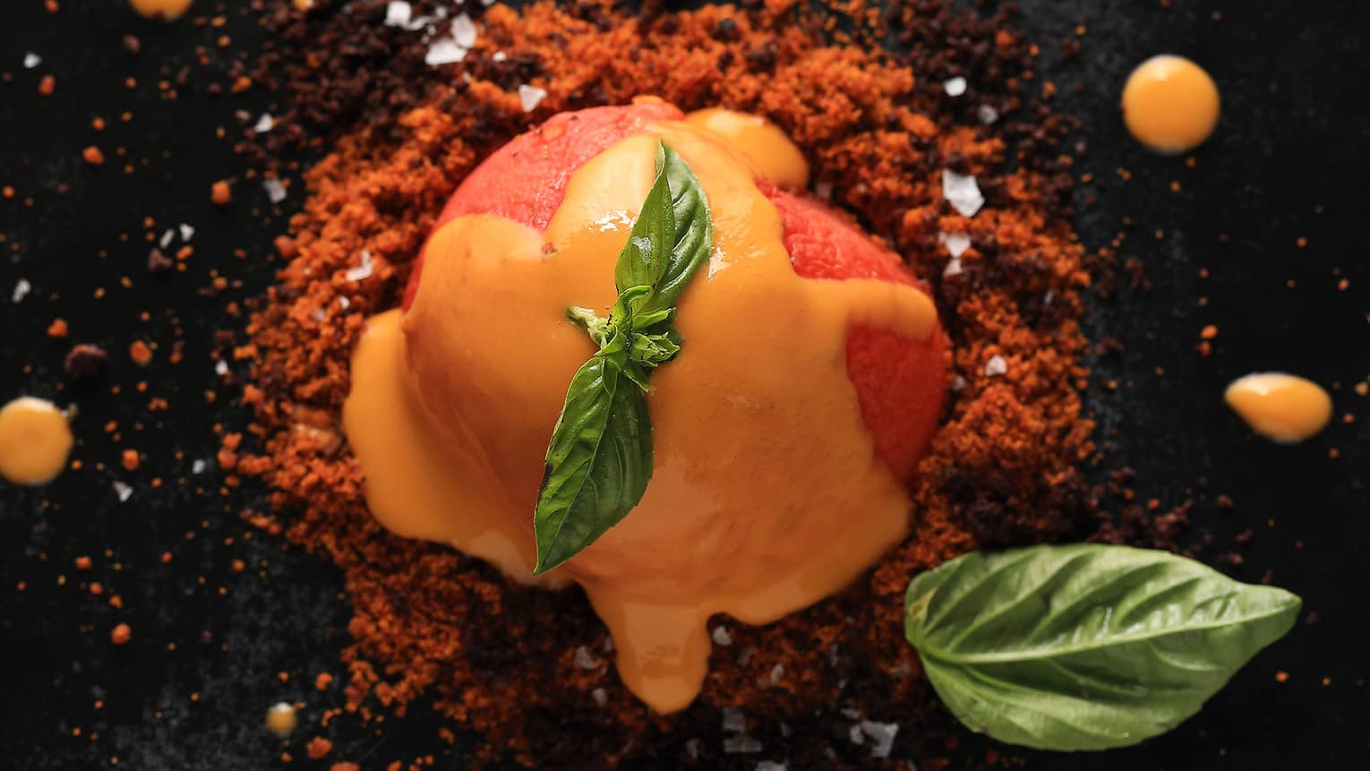 A close up of a orange sorbet like dish covered in an orange sauce and garnished with mint 