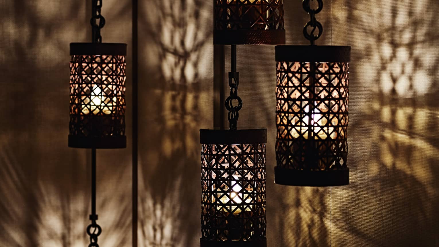 Close-up of black lanterns hanging from chains, light reflected on walls