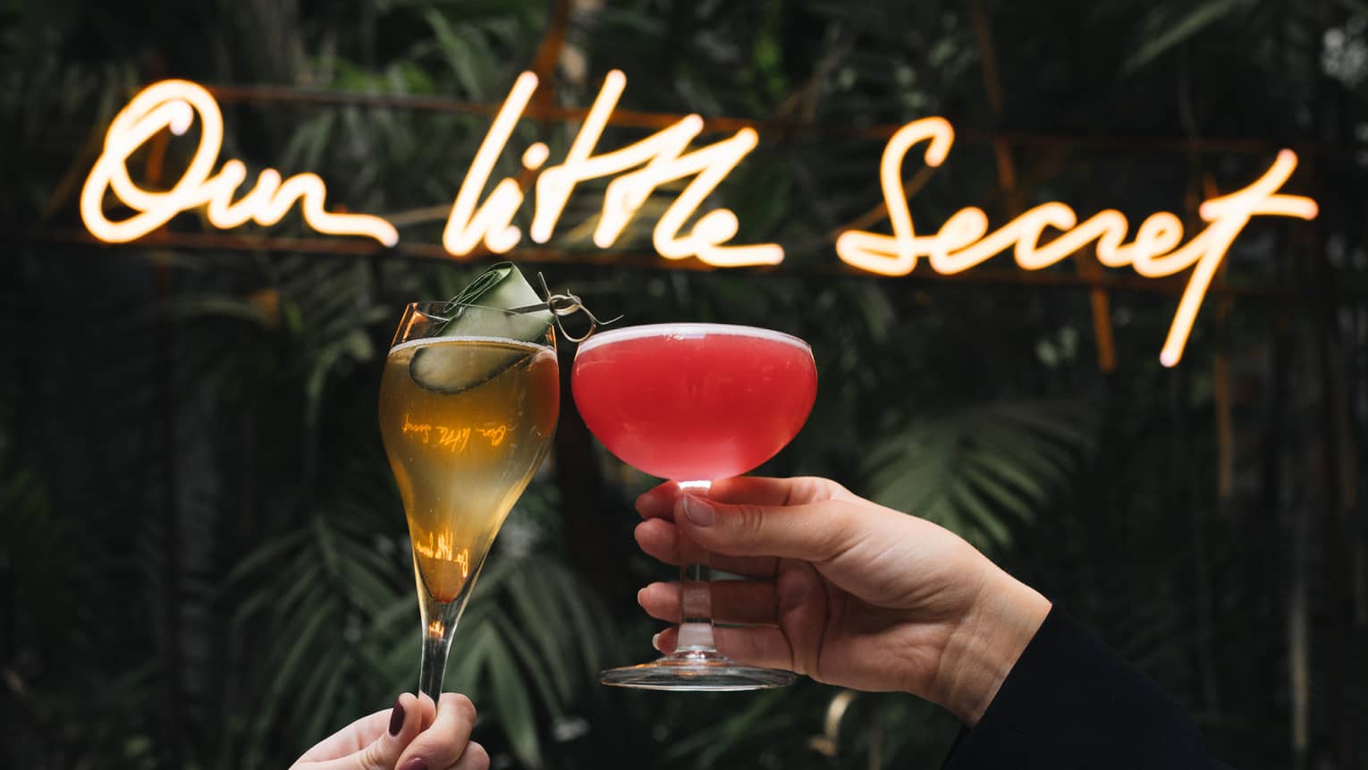 Two people toasting in front of a sign that says "our little secret."