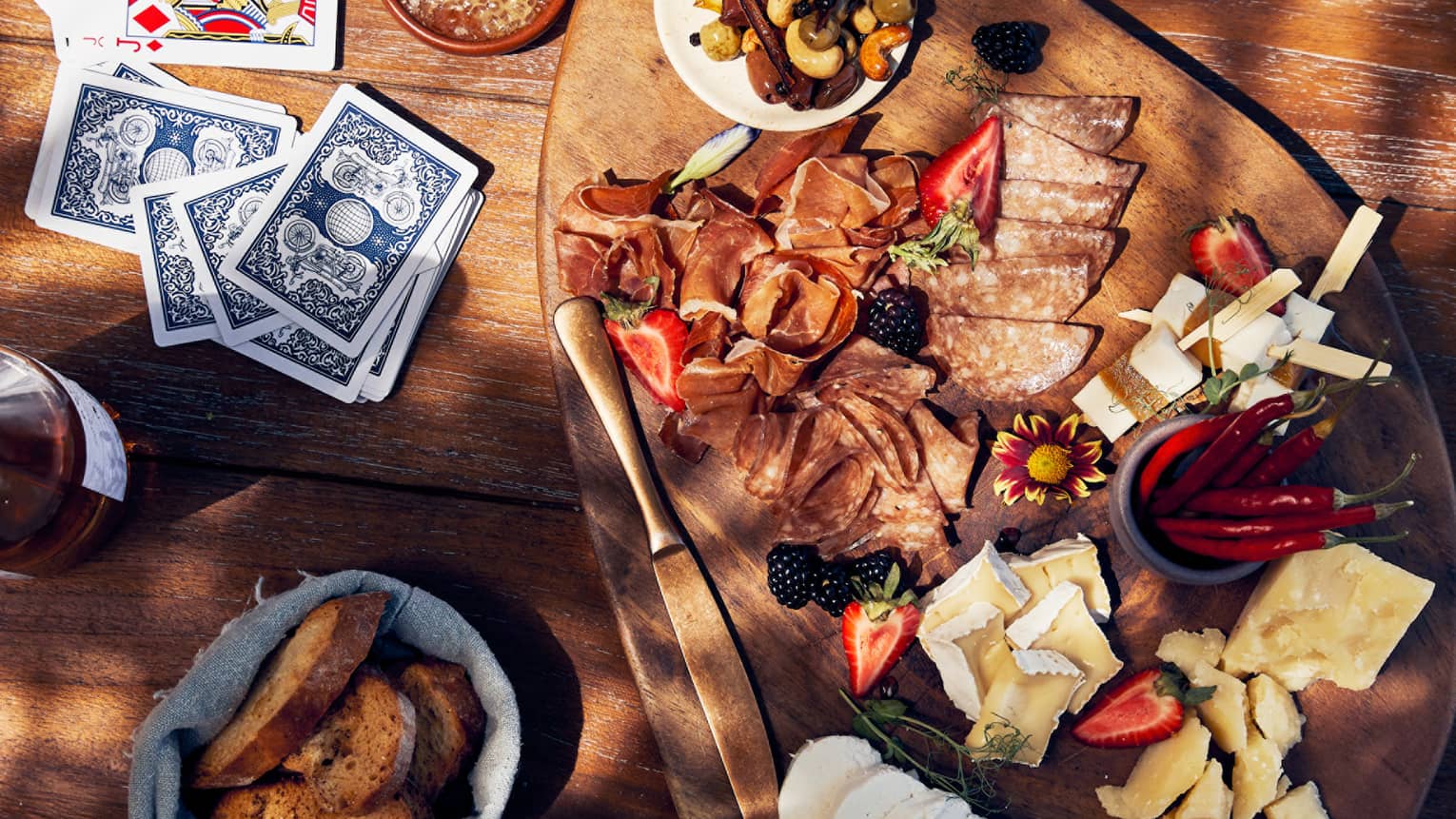 An assortment of cheese and bread and drinks on a table with playing chards.