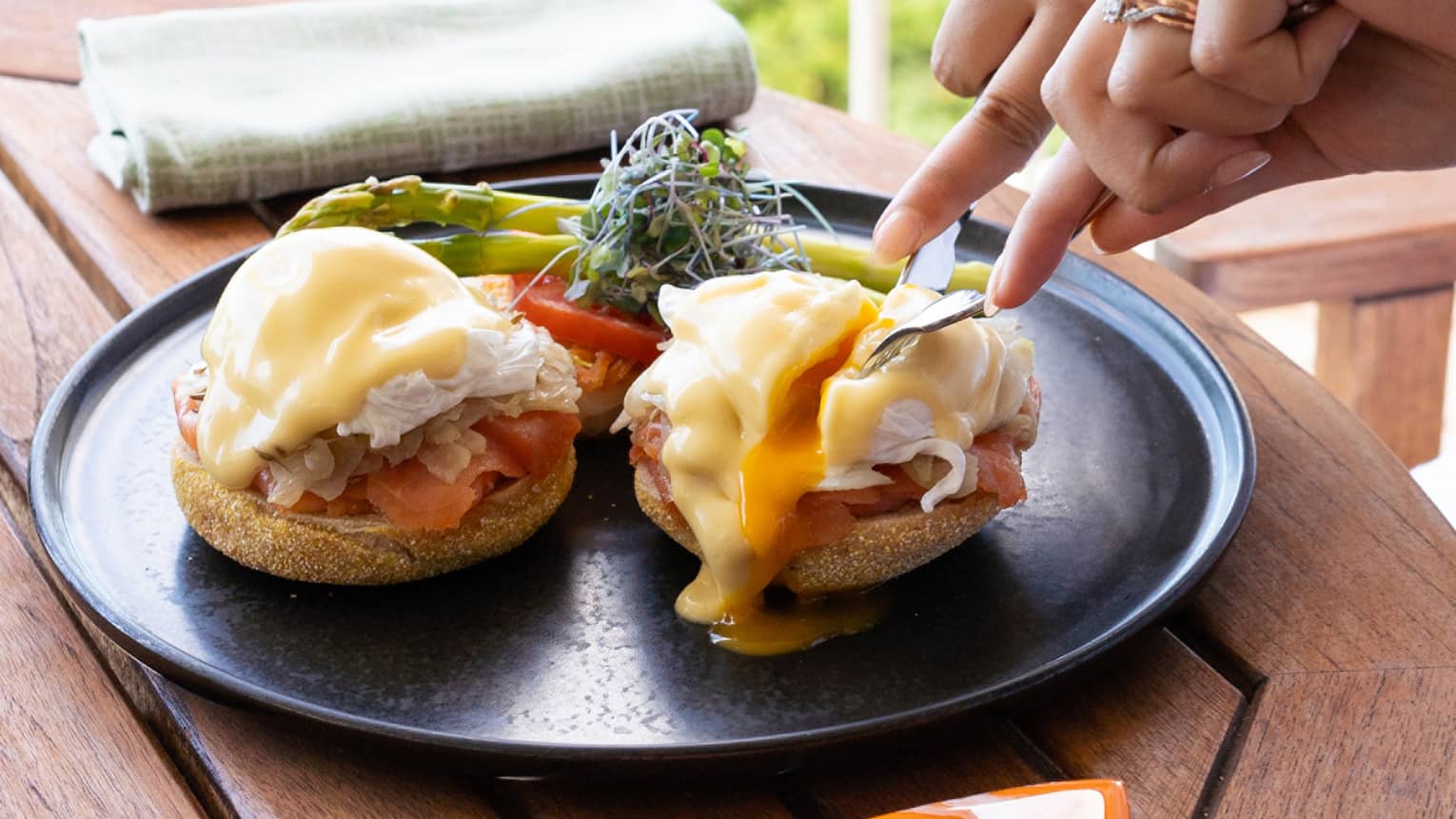A person slices into an Eggs Benedict on an outdoor hotel terrace