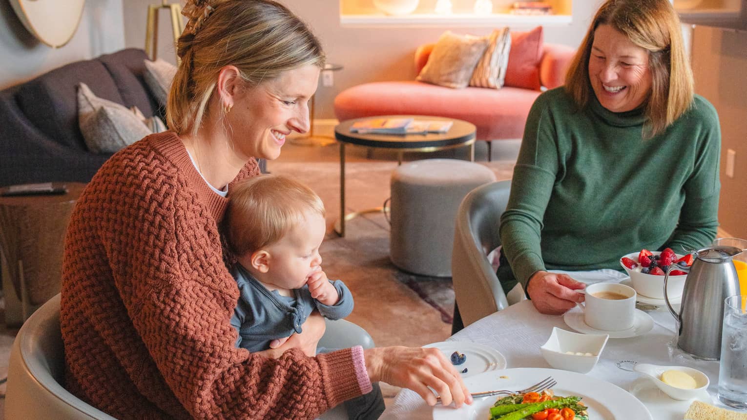 Two adults and a toddler sit at an In-Room Dining table set for a meal.