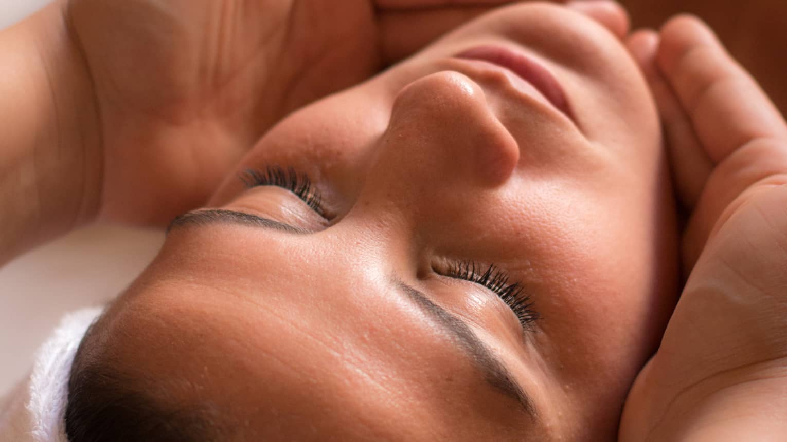 Close-up of woman with eyes closed facing up as hands cup her face and chin
