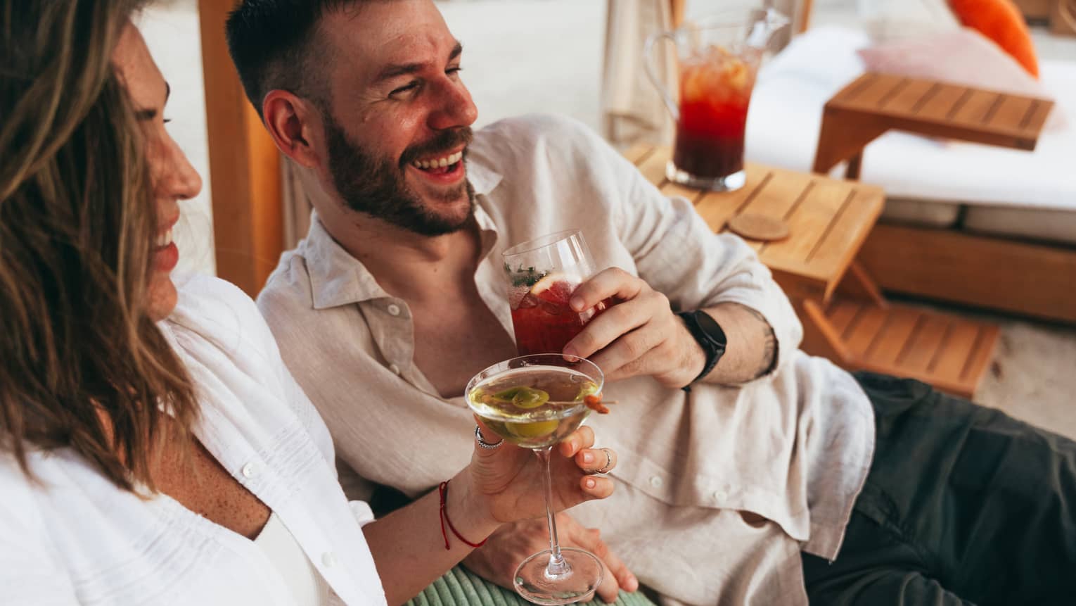 Couple sits close together in a beach cabana each enjoying a drink