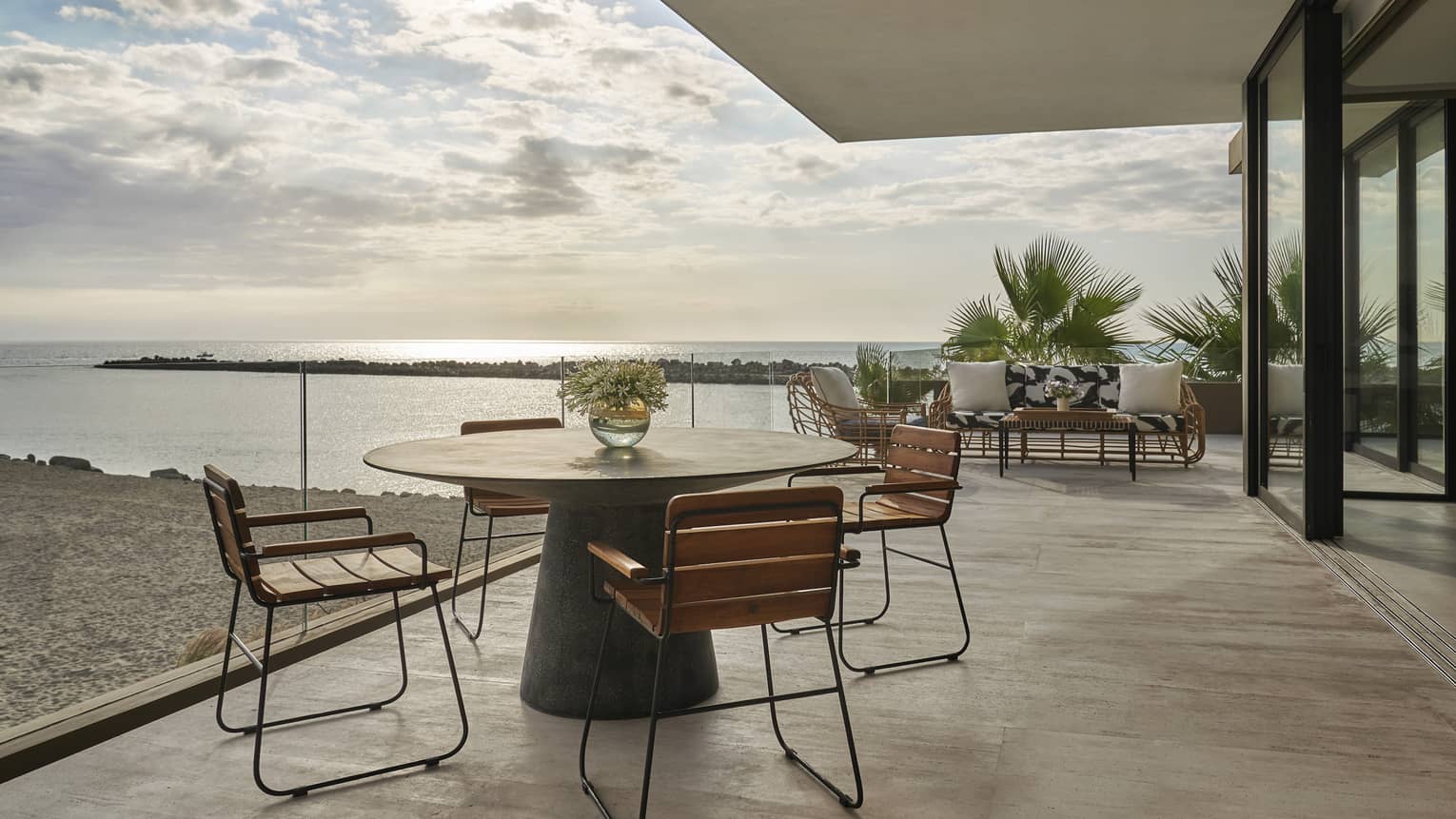 Two Bedroom Sunrise Suite deck with round table and four chairs, sofa in background, ocean views