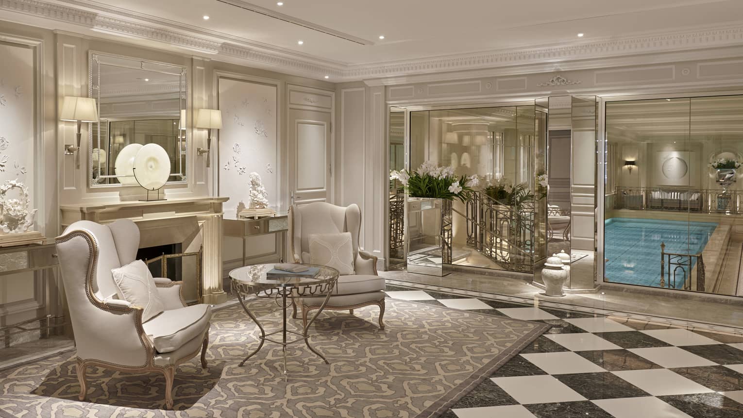 Spa lobby with two white wing chairs on beige rug, black-white checkerboard floor, view of indoor pool