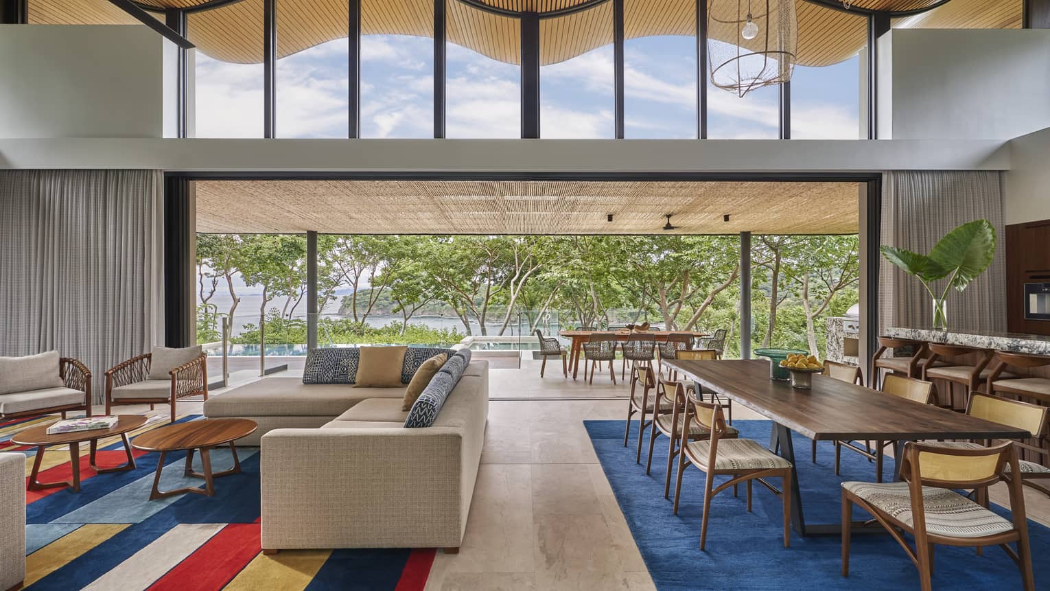Large great room with tan sectional sofa, colourful rug, wooden dining table with eight chairs