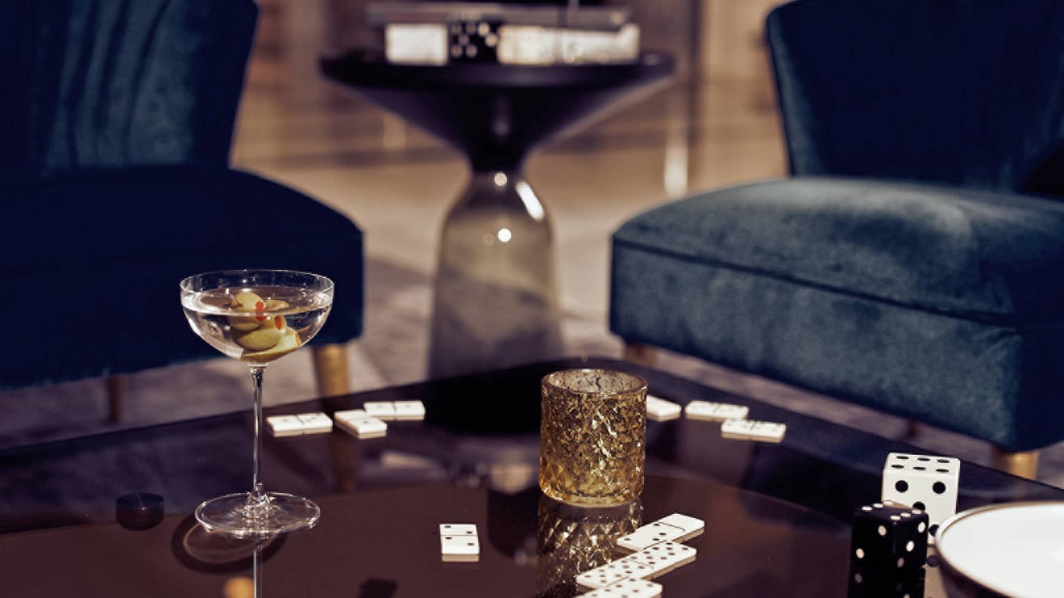 A cocktail next to dominos on a brown table.