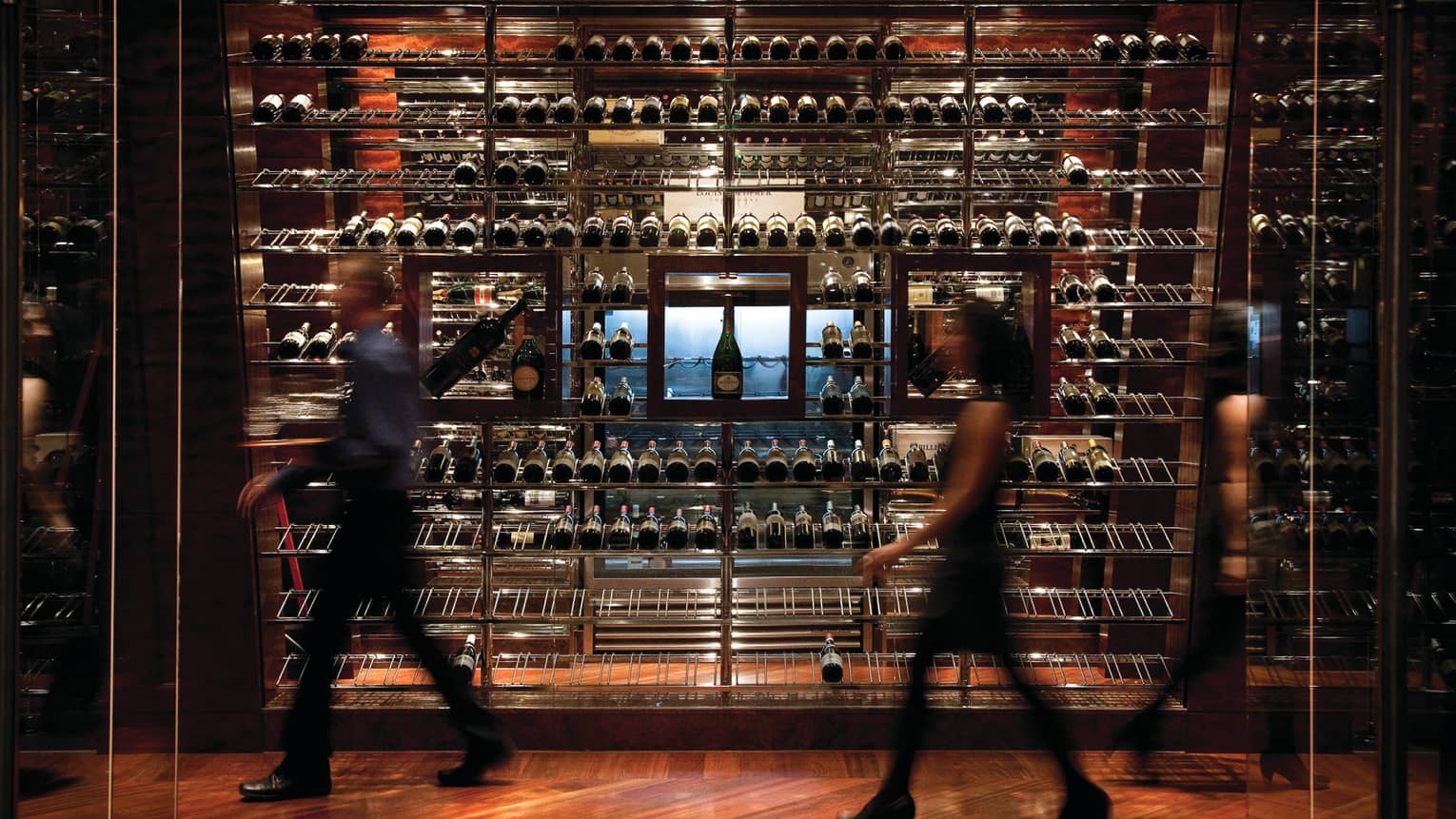 Man and woman walk by dark wine cellar display wall