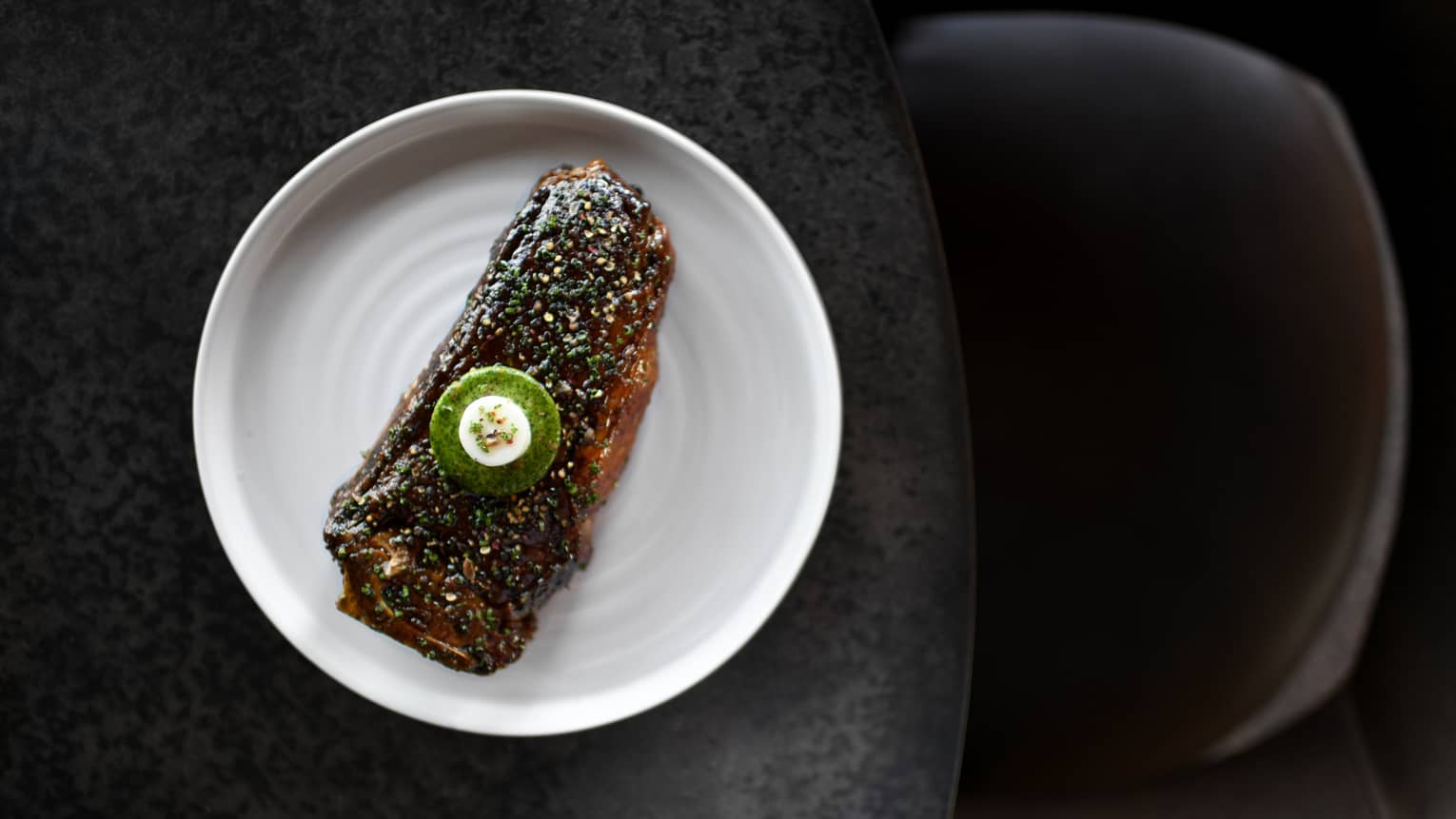 Food with a green sauce on a white plate and dark table.