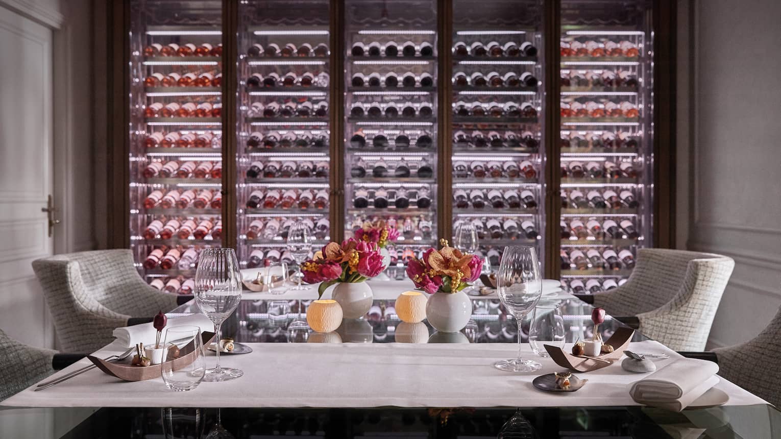 A private dining room with two chairs and an illuminated wall of wine on display