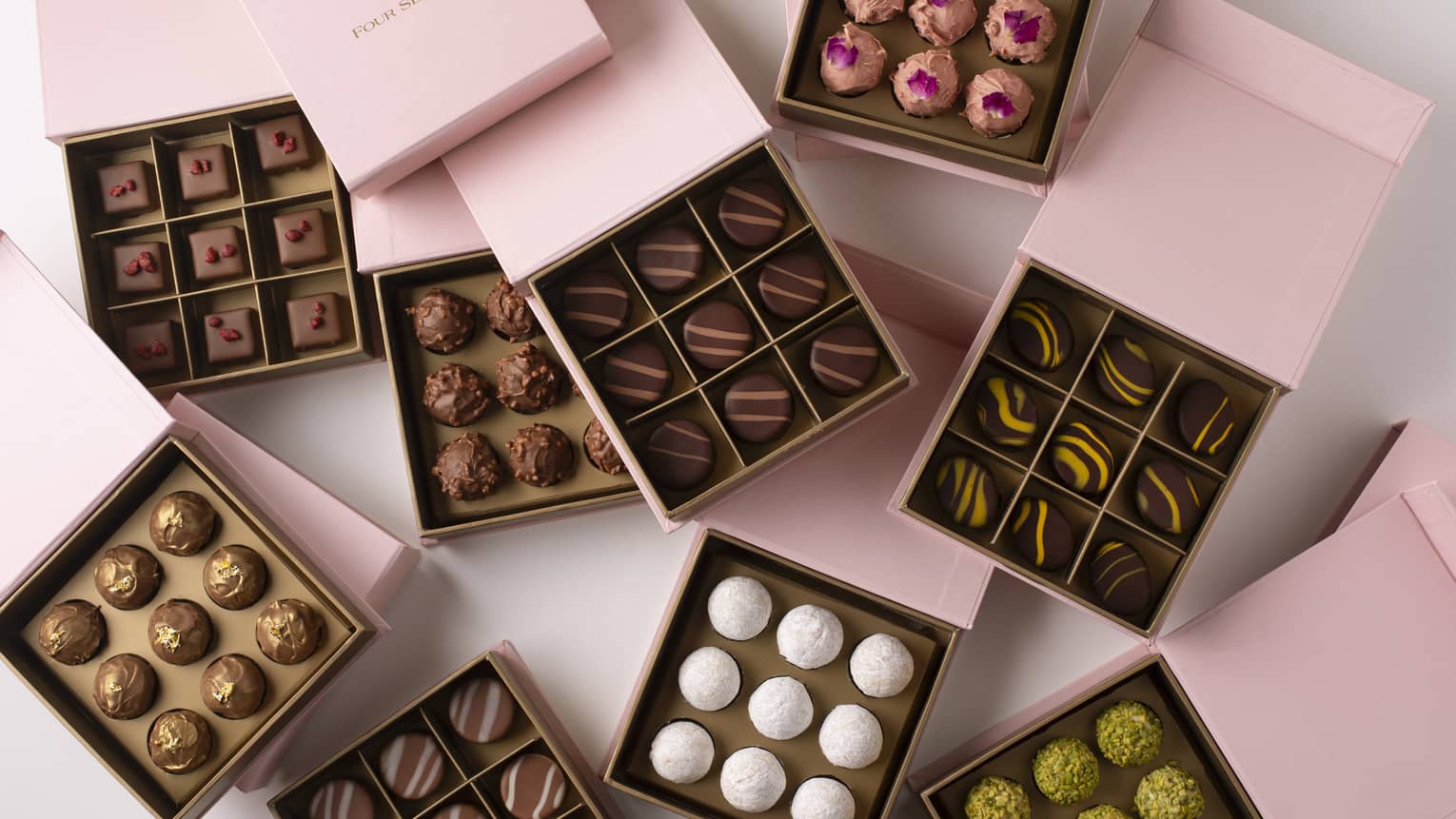 Nine square, pink boxes set on a white background, each open to reveal nine chocolate truffles within, each a different kind