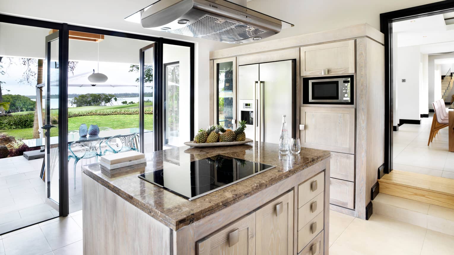 Stove range on marble island in bright, modern kitchen with open glass walls