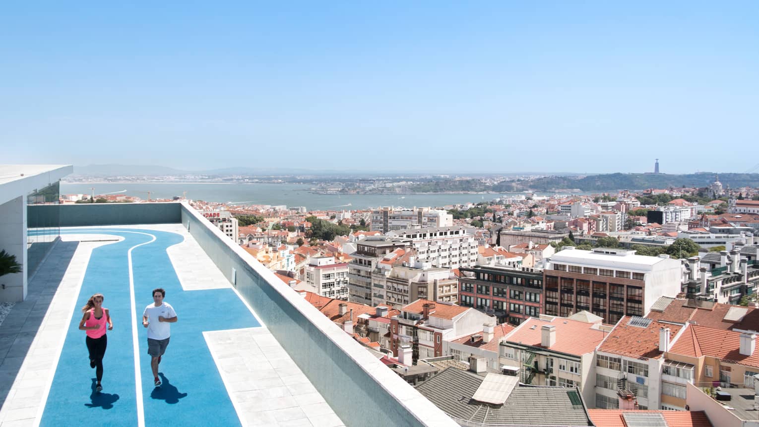 Two people run on blue, rooftop running track, overlooking Lisbon