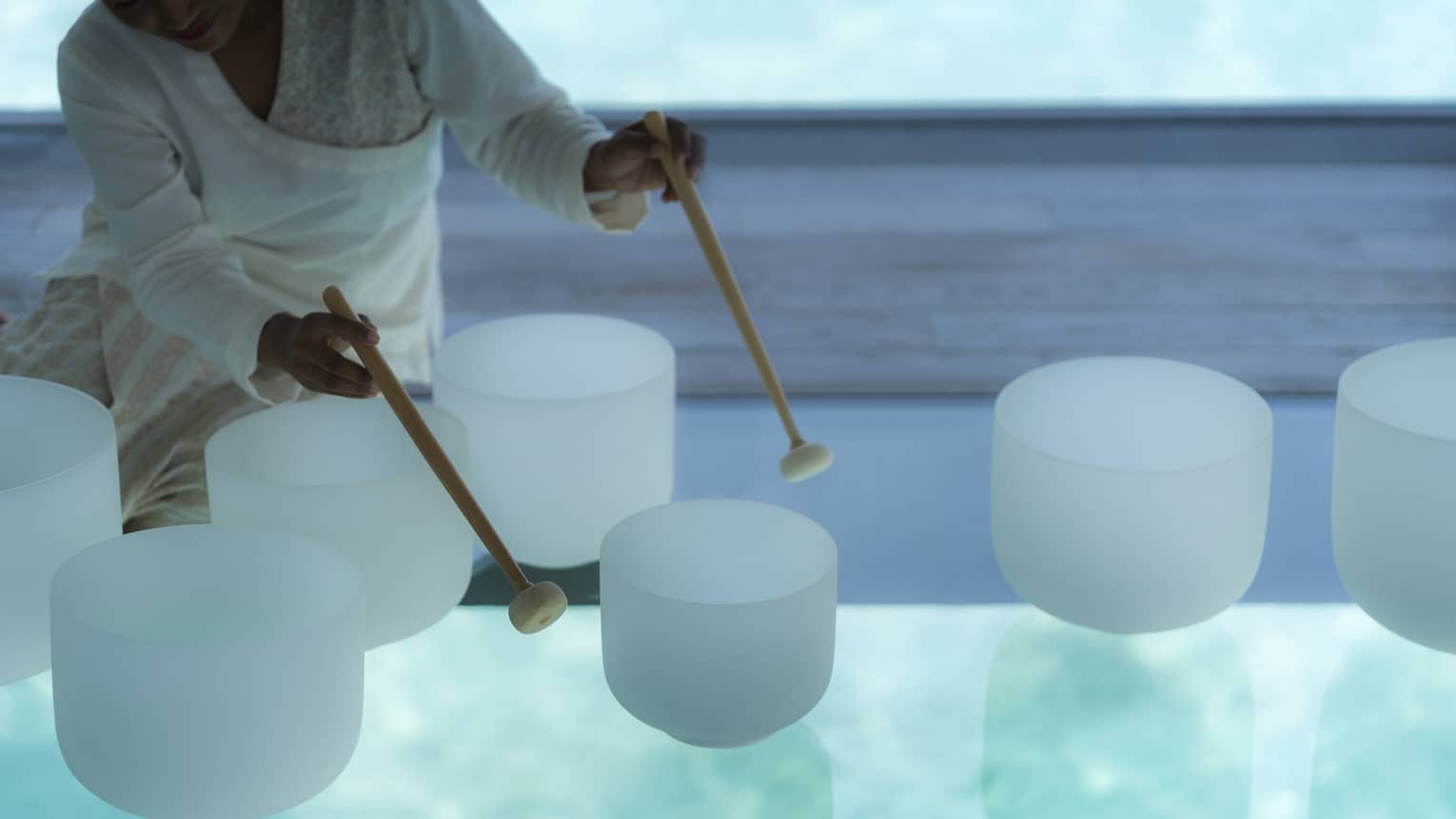 Spa staff plays various white crystal bowls with wood mallets during sound healing session